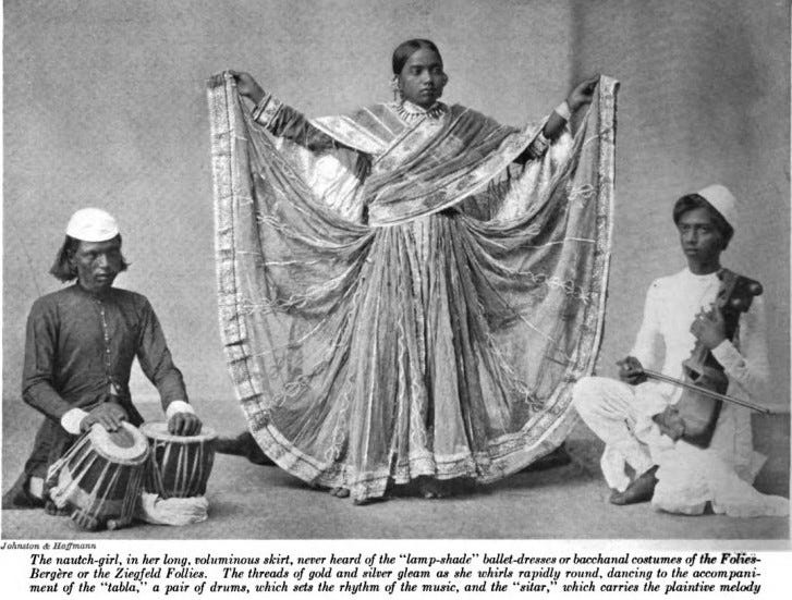 A picture of a woman in huge skirts lifting the edges of her skirt and dancing with a tabla player to her left and a sarangi player to her right. A picture of a woman in huge skirts lifting the edges of her skirt and dancing with a tabla player to her left and a sarangi player to her right.