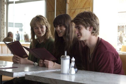 This may contain: three young people sitting at a table with an open book