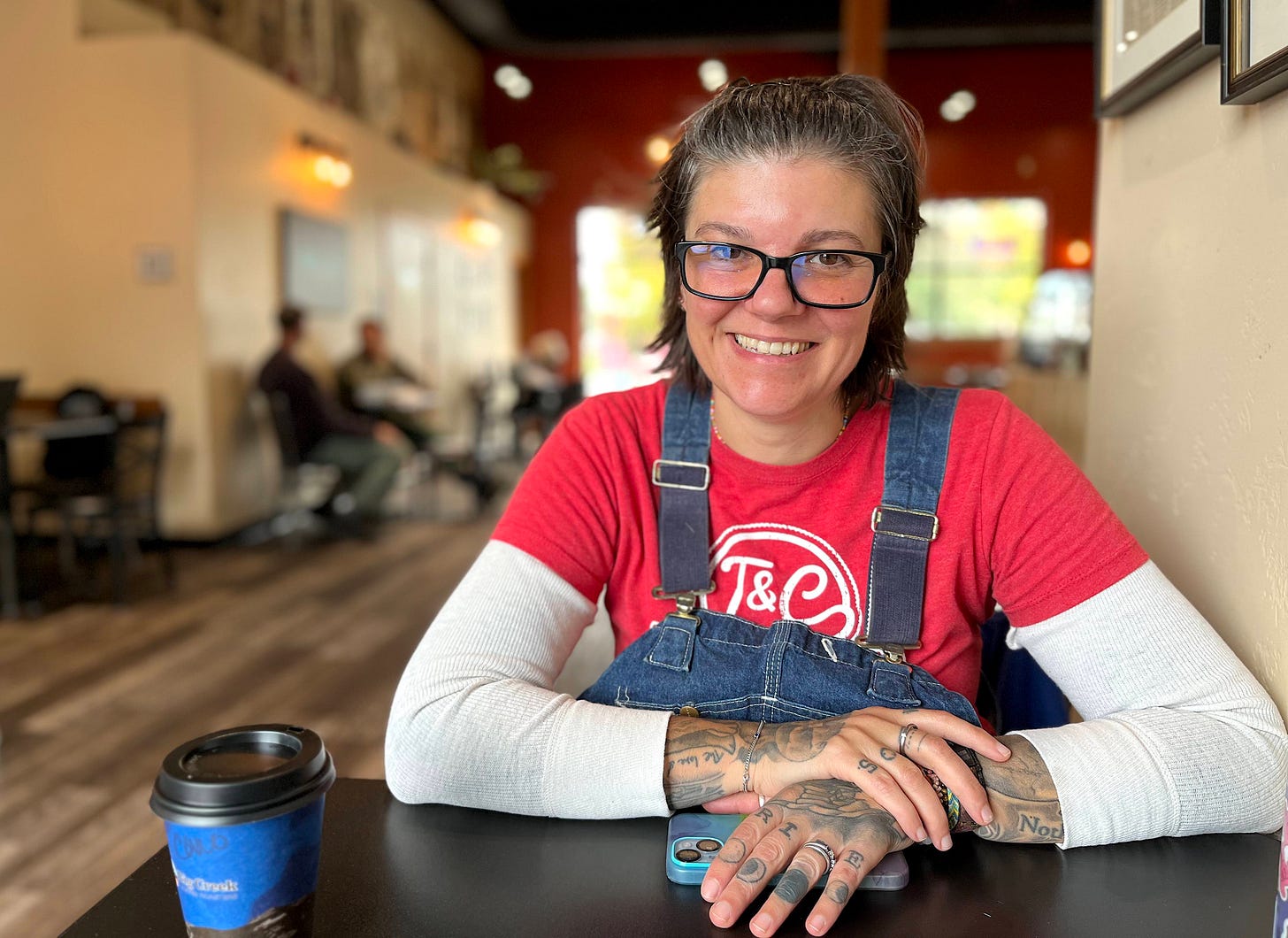 woman in overalls and glasses smiling in coffee shop