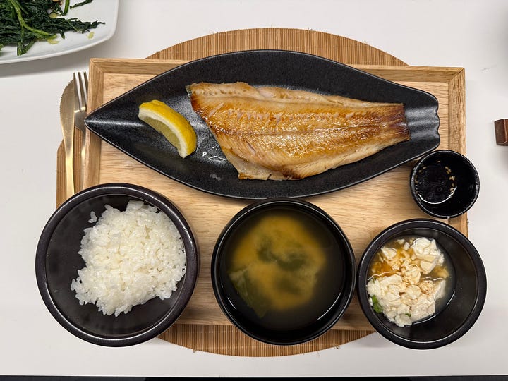 Four images of a traditional Korean and Japanese breakfast spread — grilled mackerel, rice congee with scallions, an assortment of banchan side dishes, and miso soup with tofu.