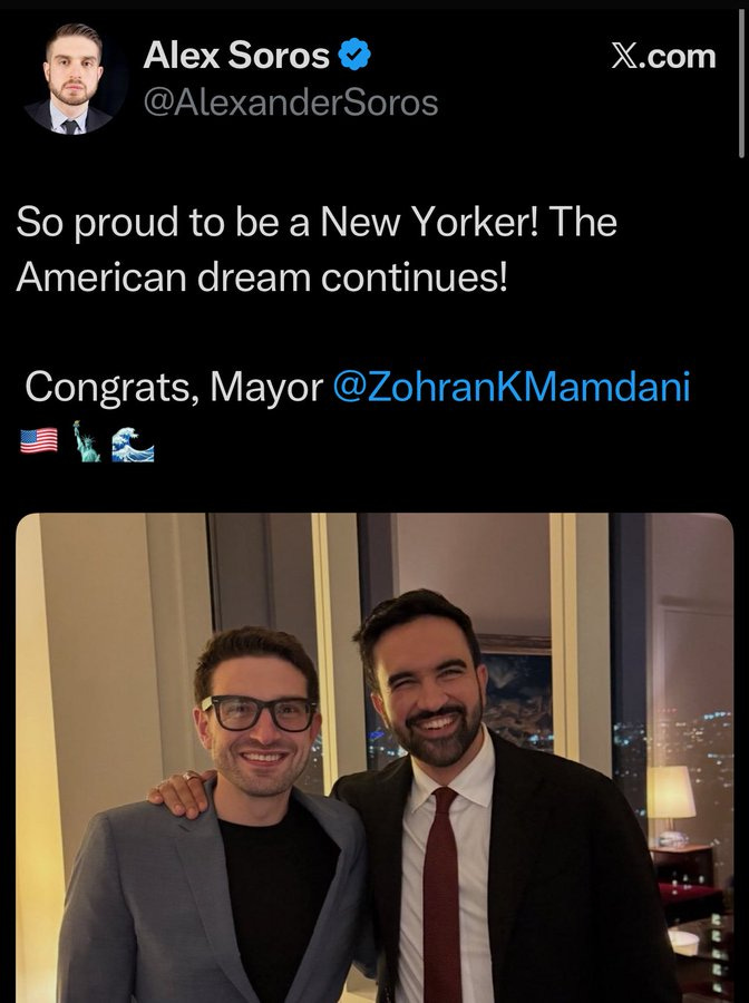 Screenshot of a tweet interface showing profile picture of a man in suit, username AlexanderSoros, verified badge, tweet text So proud to be a New Yorker The American dream continues with congratulatory message to Mayor Zohran Mamdani, American flag and New York flag emojis, below it a photo of two men one with glasses in gray suit black shirt and another in red tie dark suit smiling with arms around each other standing indoors near window with city lights at night.