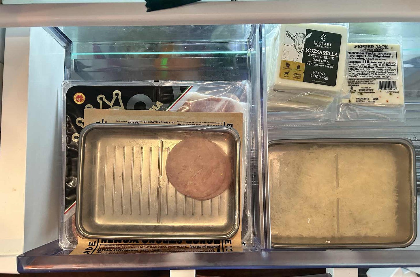 Stainless steel containers with clear lids stacked in a refrigerator drawer, one open and filled with freshly grated cheese. Stainless steel containers with clear lids stacked in a refrigerator drawer, one open and filled with freshly grated cheese.