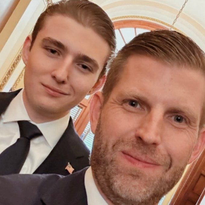 A selfie of two men in suits against the backdrop of an interior with windows and decorated walls.