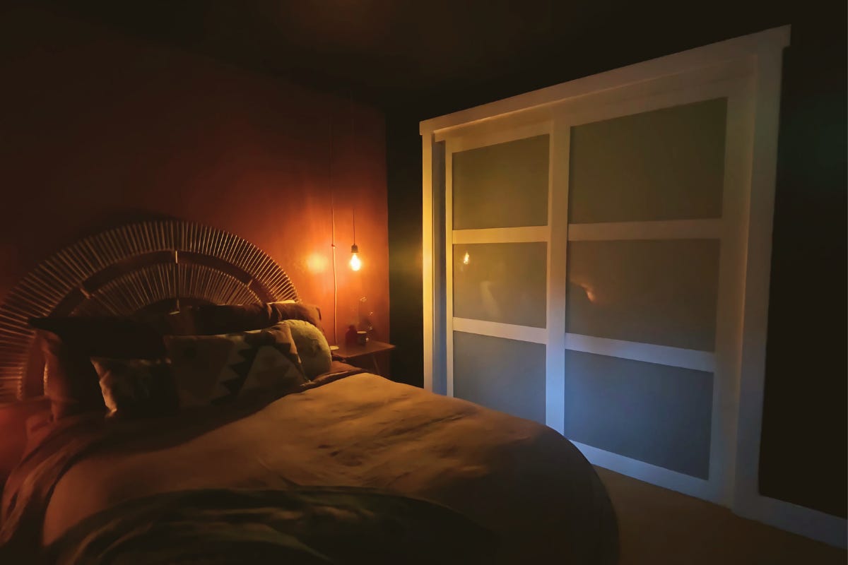 A moody bedroom with dark red walls, a large rattan headboard, and a single Edison bulb hanging over the nightstand, casting a warm glow. A moody bedroom with dark red walls, a large rattan headboard, and a single Edison bulb hanging over the nightstand, casting a warm glow.