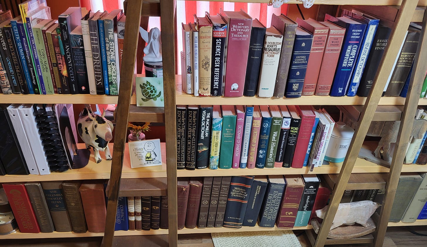 A large, wooden bookshelf filled with vintage dictionaries, encyclopedias, and reference books, flanked by two wooden ladders. Titles include works on mythology, Celtic traditions, and word origins. A ceramic cow figurine, a Snoopy quote card, and a leafy hand-painted tile add whimsy to the scholarly collection. Soft red curtains glow in the background, giving the cozy reading nook a warm, inviting feel. A large, wooden bookshelf filled with vintage dictionaries, encyclopedias, and reference books, flanked by two wooden ladders. Titles include works on mythology, Celtic traditions, and word origins. A ceramic cow figurine, a Snoopy quote card, and a leafy hand-painted tile add whimsy to the scholarly collection. Soft red curtains glow in the background, giving the cozy reading nook a warm, inviting feel.