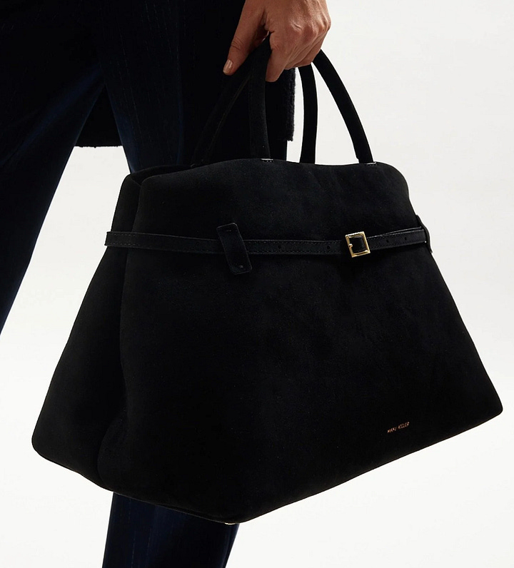 suede leather tote bag with gold buckle detail like the row bag featuring short borwn handles and gold and red trendy bag charm with polished gold hardware and branding
