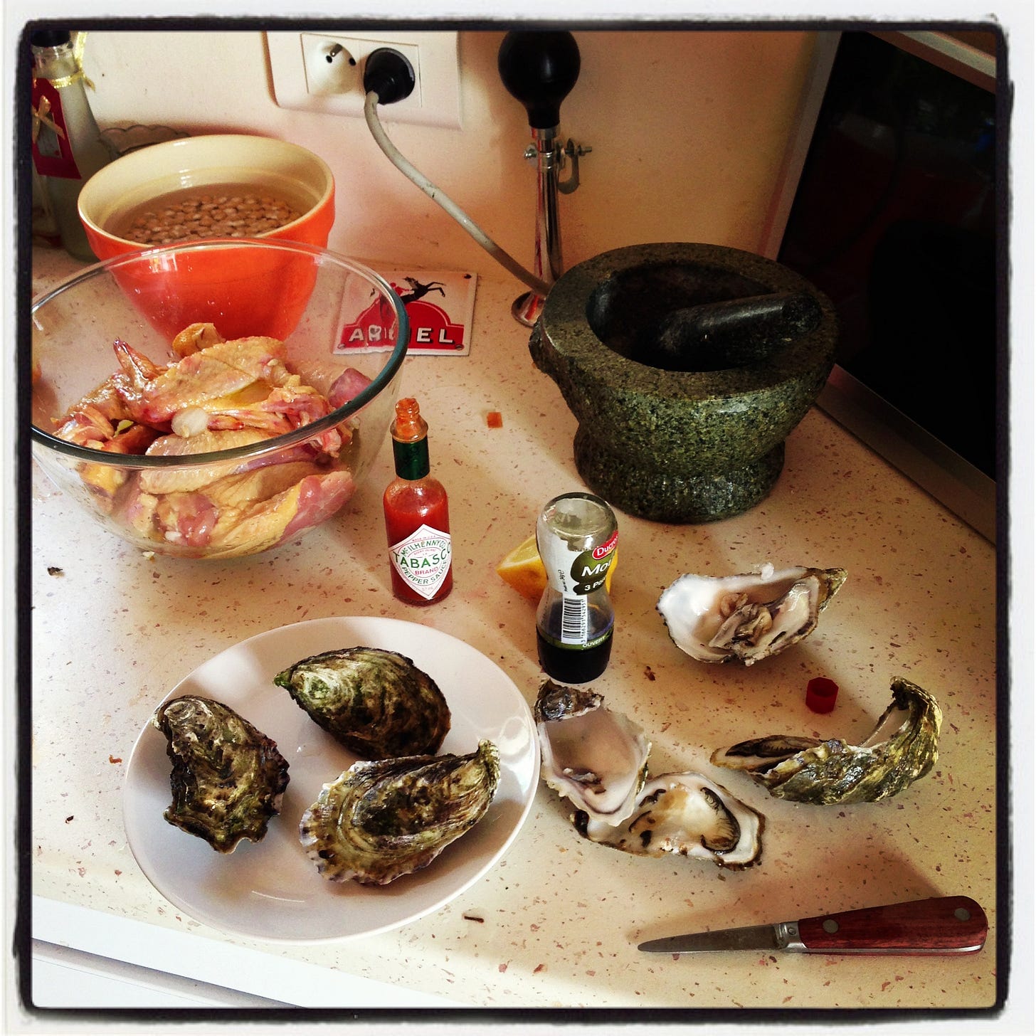 Oysters, tobasco, chicken thighs and beans soaking in an orange bowl