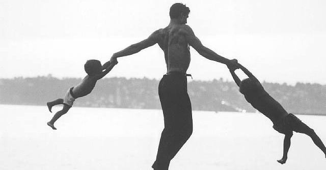 This may contain: a man and two children are playing with each other on the beach by the water