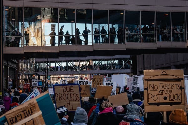 People holding cardboard signs stand outside glass walkways connecting buildings.