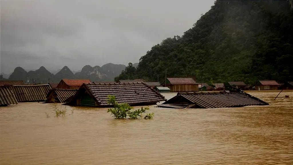 Floodwaters submerge rooftops in a rural area of central Vietnam, with only the tops of houses visible above the muddy water as heavy rain and landslides continue to inundate communities surrounded by mountains.