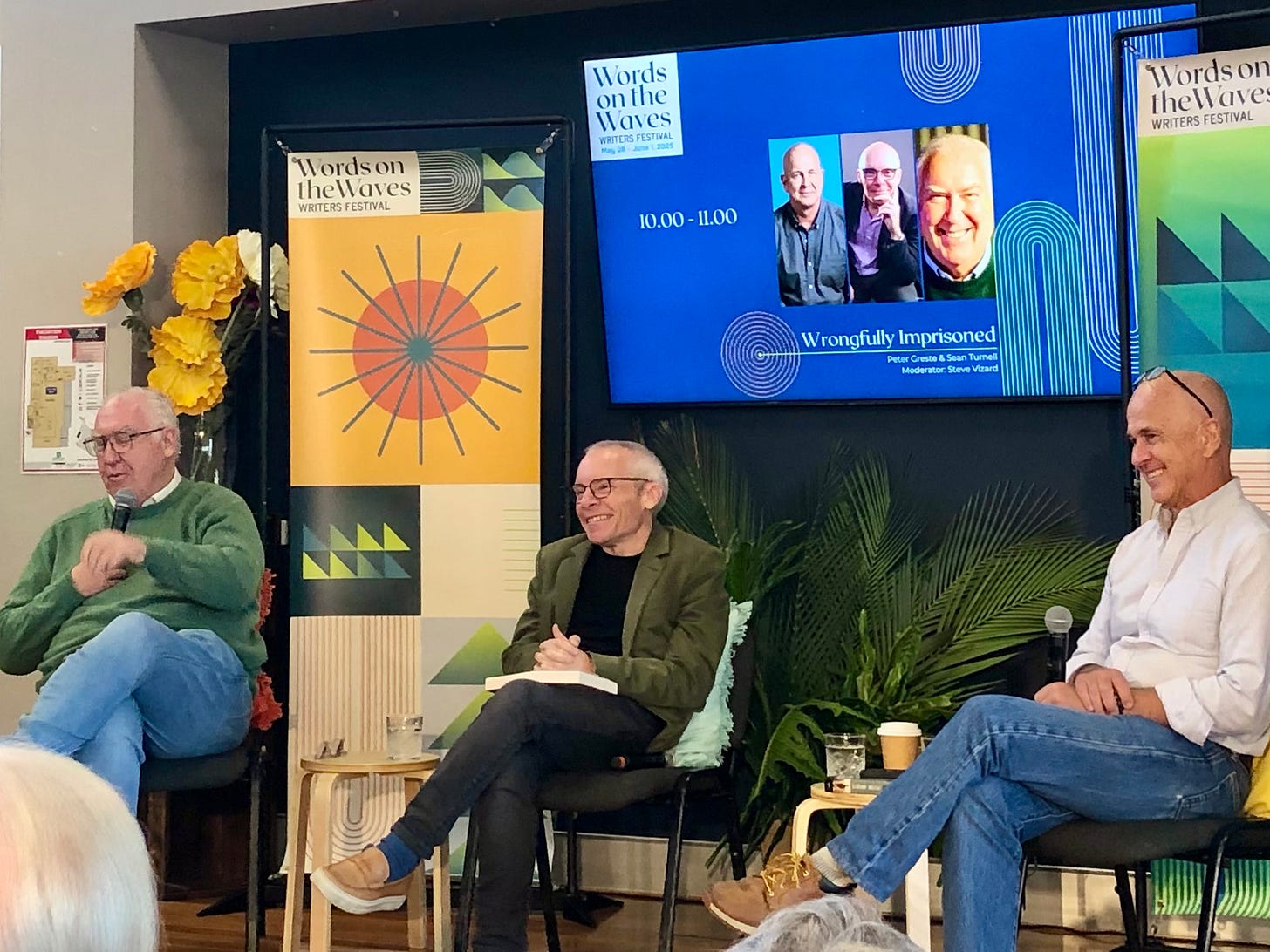 A photo of three men sitting on a stage at a writers festival