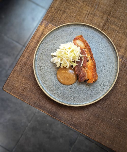A grey plate with pork belly, sauerkraut, and cider mustard on top, on top of a wooden table