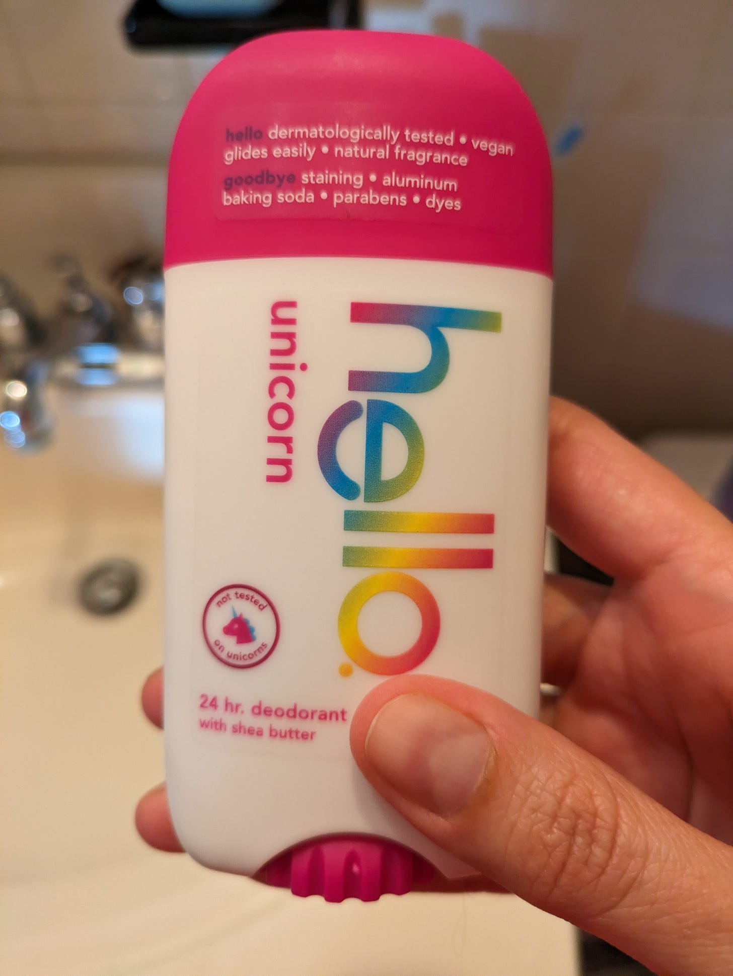 A photo of the "hello" unicorn deodorant in my hand. It has a pink cap and the text is rainbow-colored.