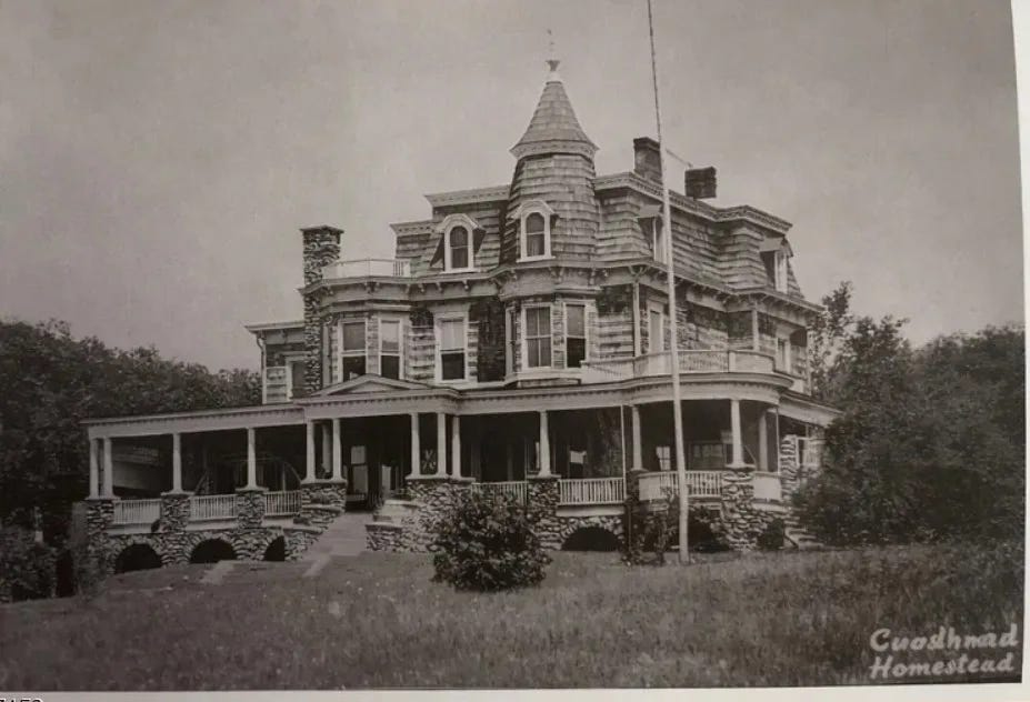Historic black-and-white photograph of a large Victorian house with a turret, dormer windows, and a broad wraparound porch supported by columns and stone foundations. The building sits on a grassy hill with trees behind it and a flagpole in front. The image shows the early Goodland House, which later became the centerpiece of Camp Goodland in New Jersey.
