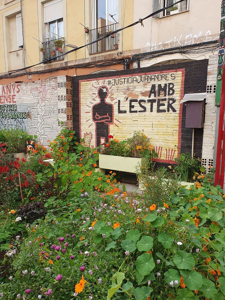 A painted wall says "#JusticiaJuanAndrés Amb L'ester", flowers are blossoming in front of it. The other image shows a small toilet bathroom with orange painted walls, flower decoration and a sign "Fascismo aquí" pointing into the toilet.