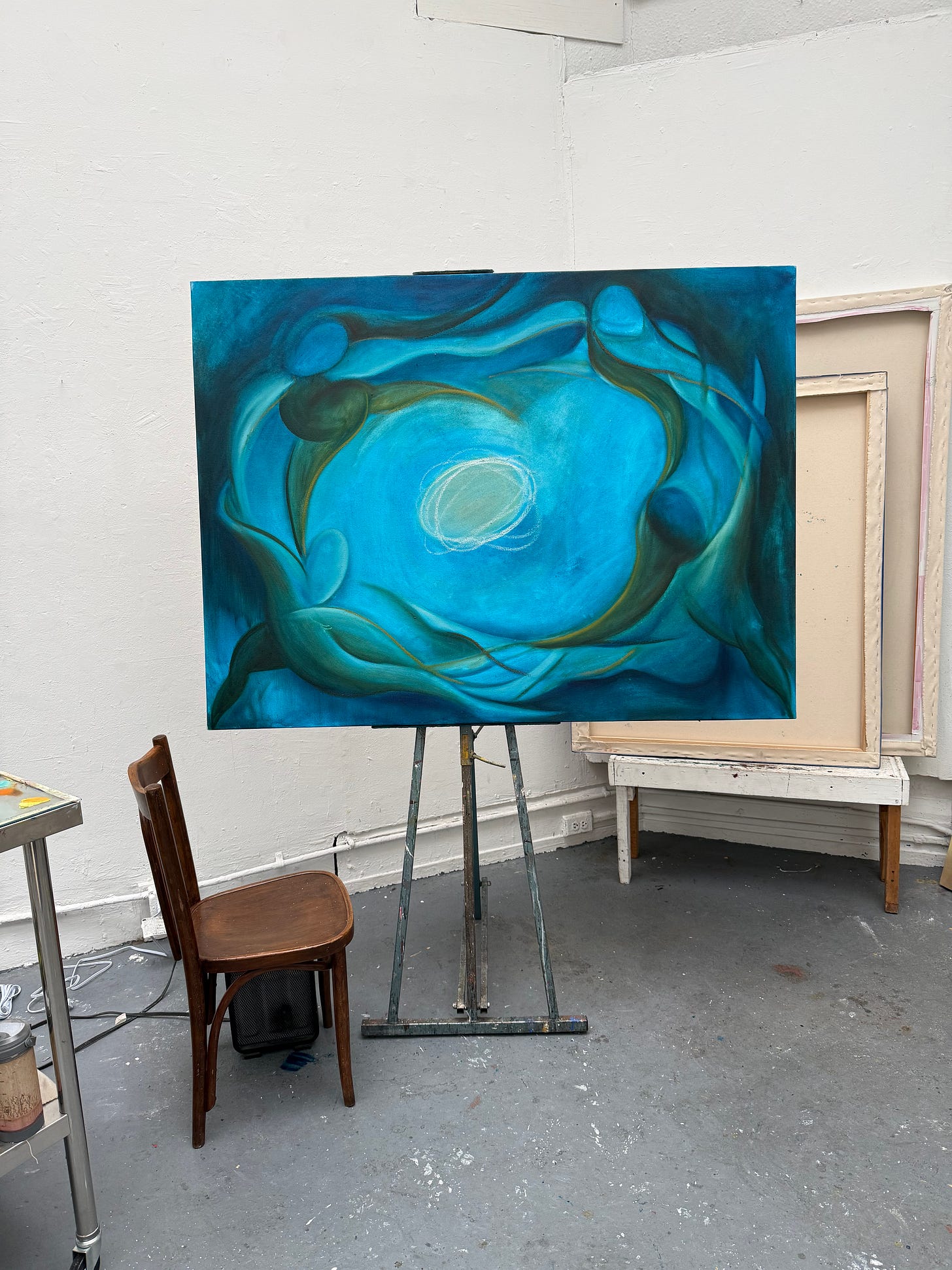 Alex Maceda’s blue-green painting baptism in progress, shown on an easel in the studio beside a wooden chair and blank stretched canvases. Alex Maceda’s blue-green painting baptism in progress, shown on an easel in the studio beside a wooden chair and blank stretched canvases.
