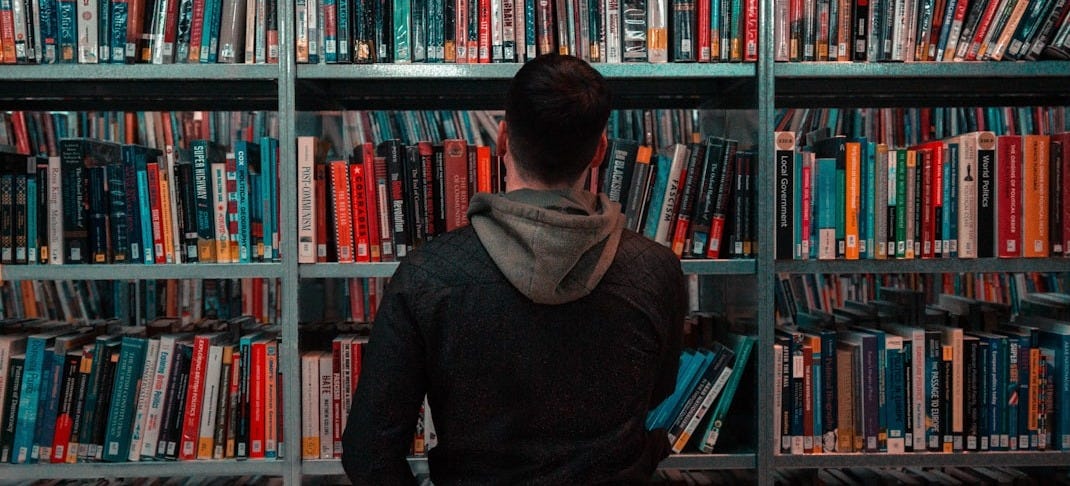 person wearing black and gray jacket in front of bookshelf