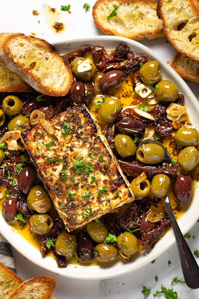 White plate filled with baked feta olives and herbs