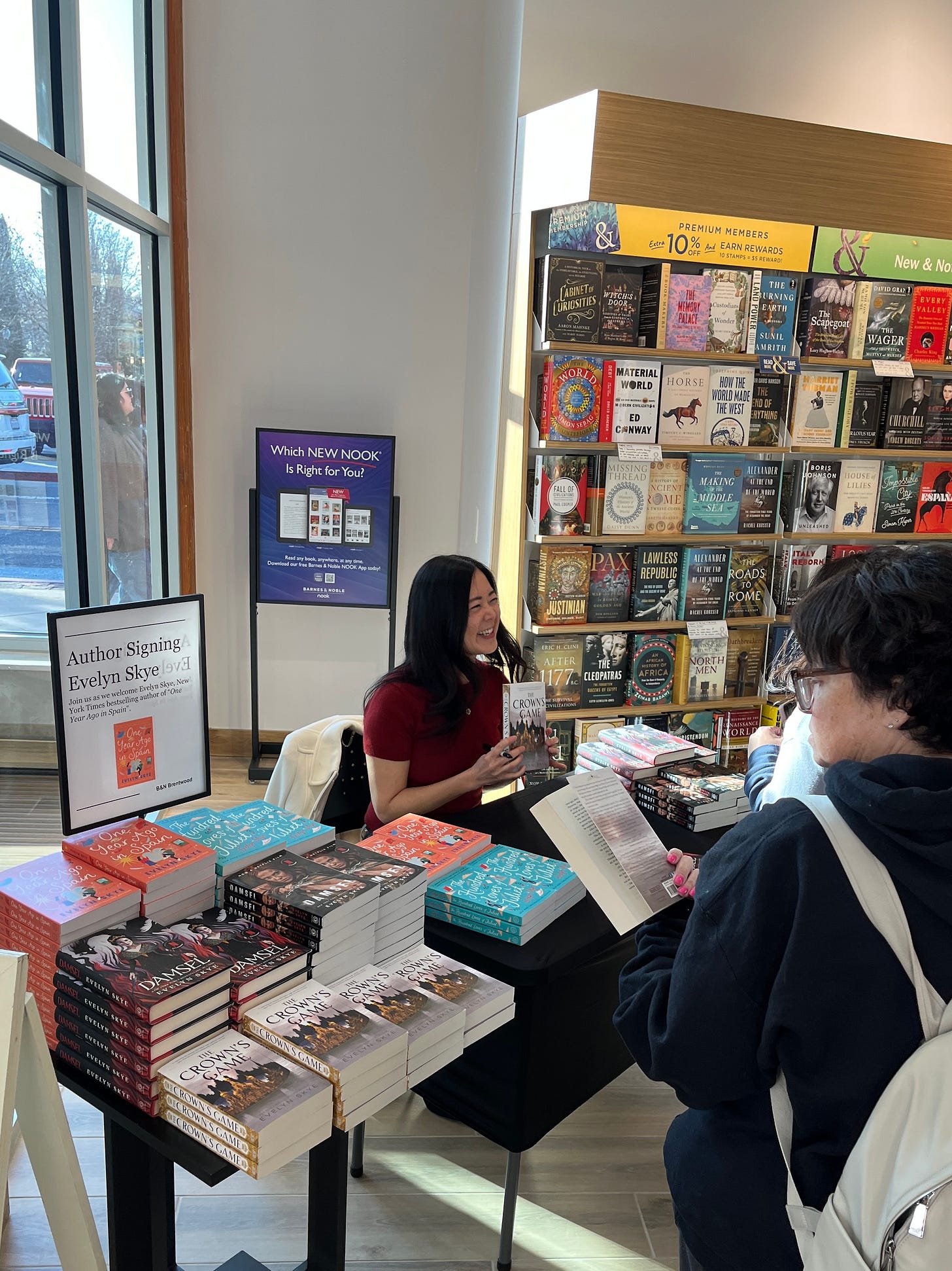 Author Evelyn Skye at Barnes & Noble, at a table with stacks of her books. She is interacting with a reader about The Crown's Game.