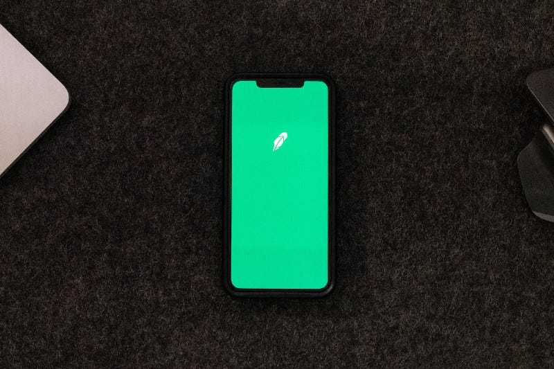 The green Robinhood app opening on a cell phone on a desk. The green Robinhood app opening on a cell phone on a desk.