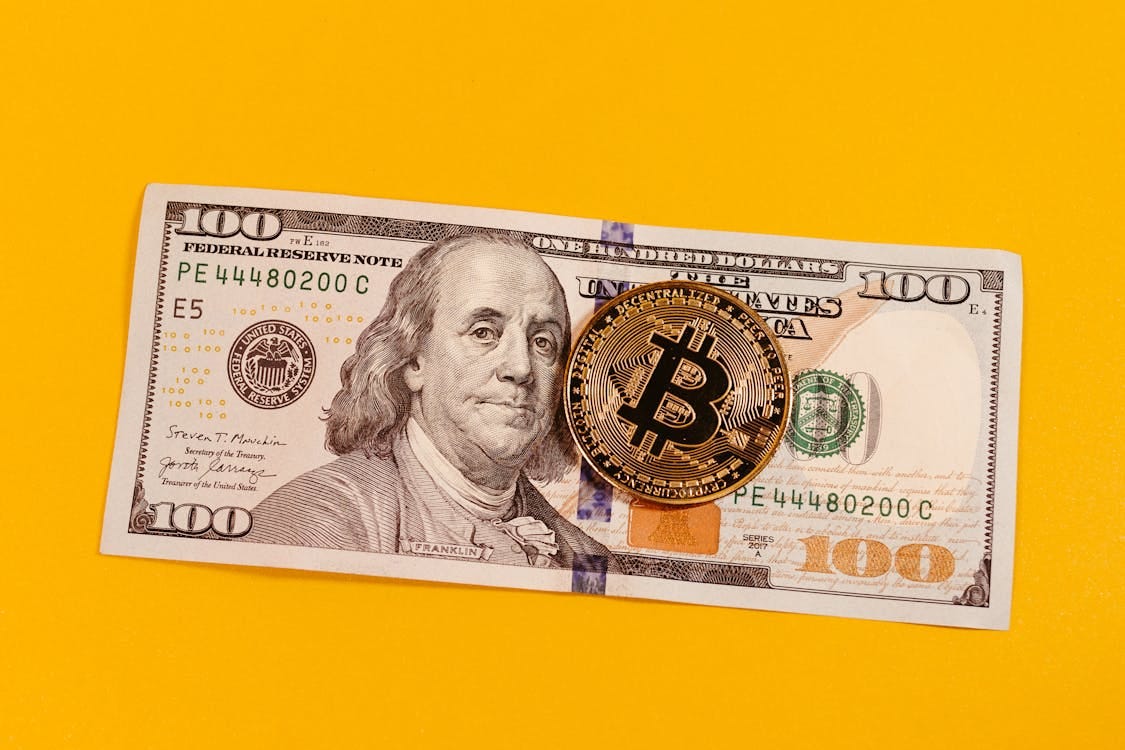 Free Gold bitcoin placed on a 100 US dollar bill over a bright yellow backdrop, symbolizing modern digital currency. Stock Photo