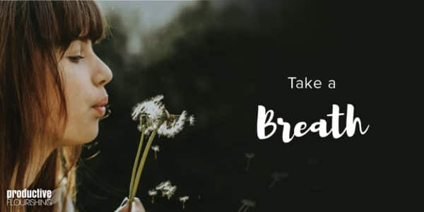 A woman blows a dandelion puff from the left-hand side of the frame. Text Overlay: Take A Breath A woman blows a dandelion puff from the left-hand side of the frame. Text Overlay: Take A Breath