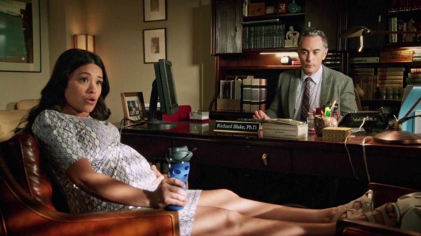 Scène de la série Jane The Virgin, où Jane est assise dans le bureau de son chef, très enceinte, et se tenant le ventre, son chef la regarde avec inquiétude.