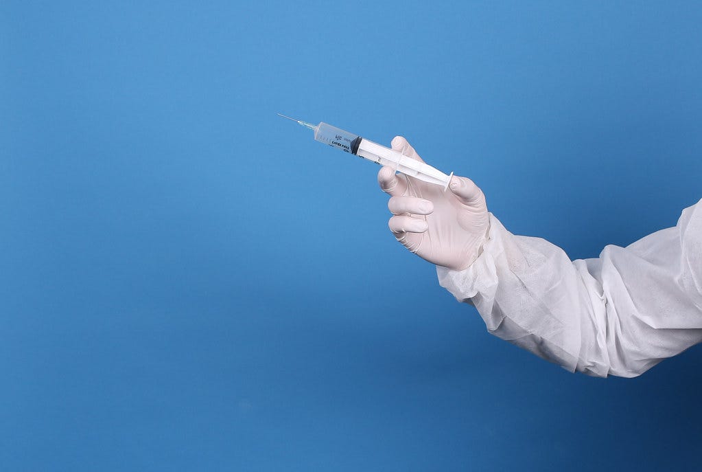 Doctor in protective suit and face mask holding syringe Doctor in protective suit and face mask holding syringe