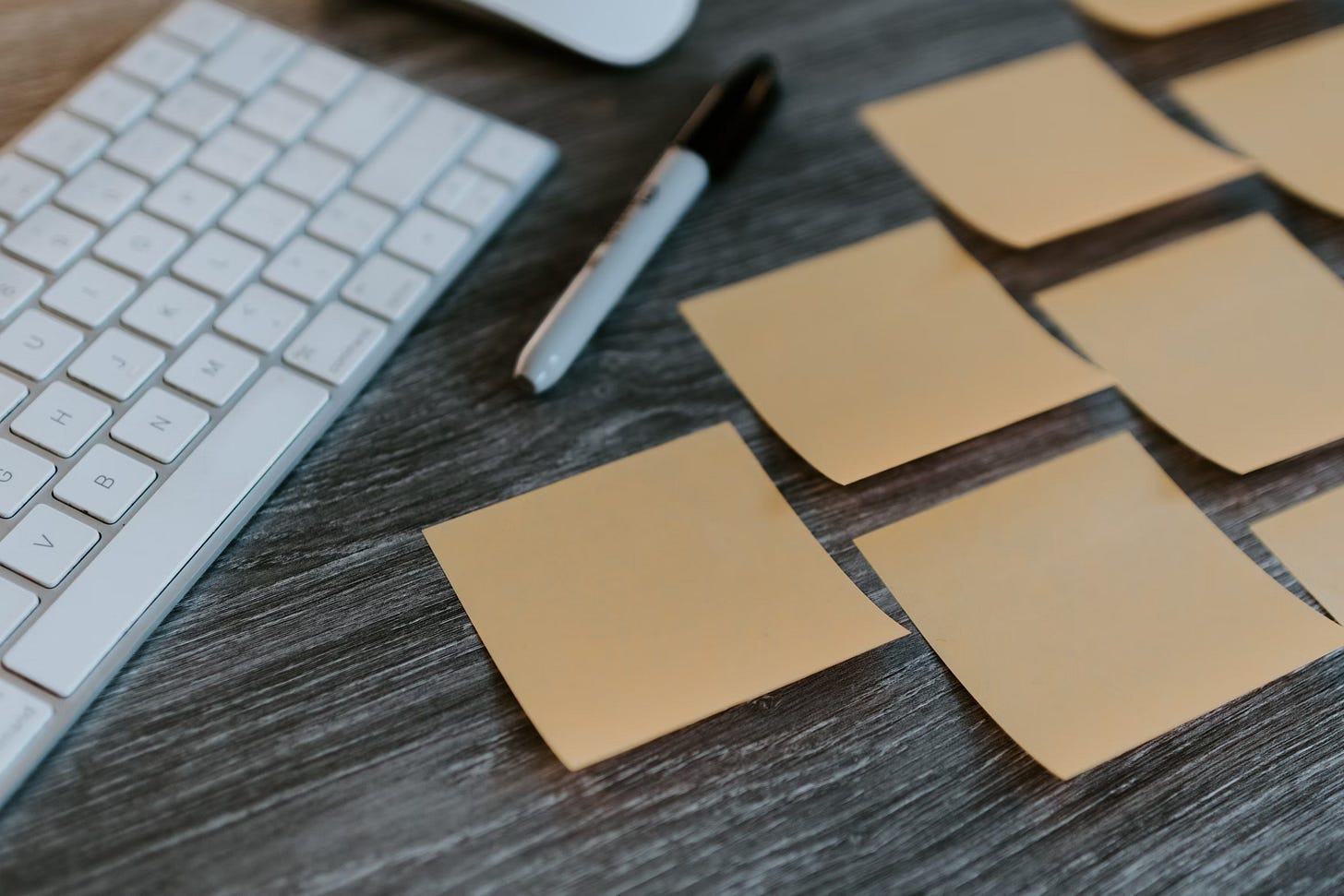 Desk area with a white keyboard, sharpie marker, and assortment of pale orange post it notes.