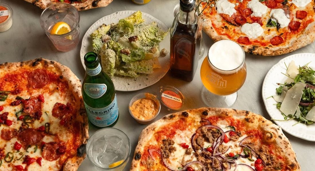 A table with pizzas, garlic bread, salads, glasses, and beer bottles on top of it A table with pizzas, garlic bread, salads, glasses, and beer bottles on top of it