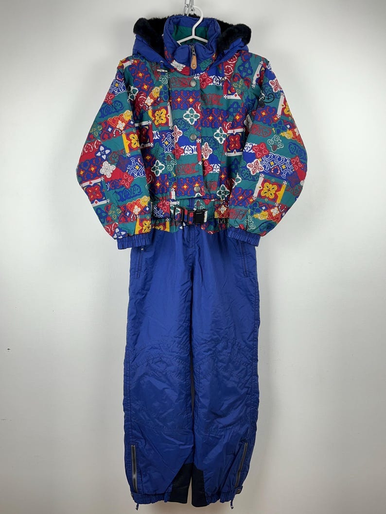 May include: A blue ski suit with a colorful geometric pattern. The suit has a hood with a black fur trim, a zipper closure, and a belt at the waist.