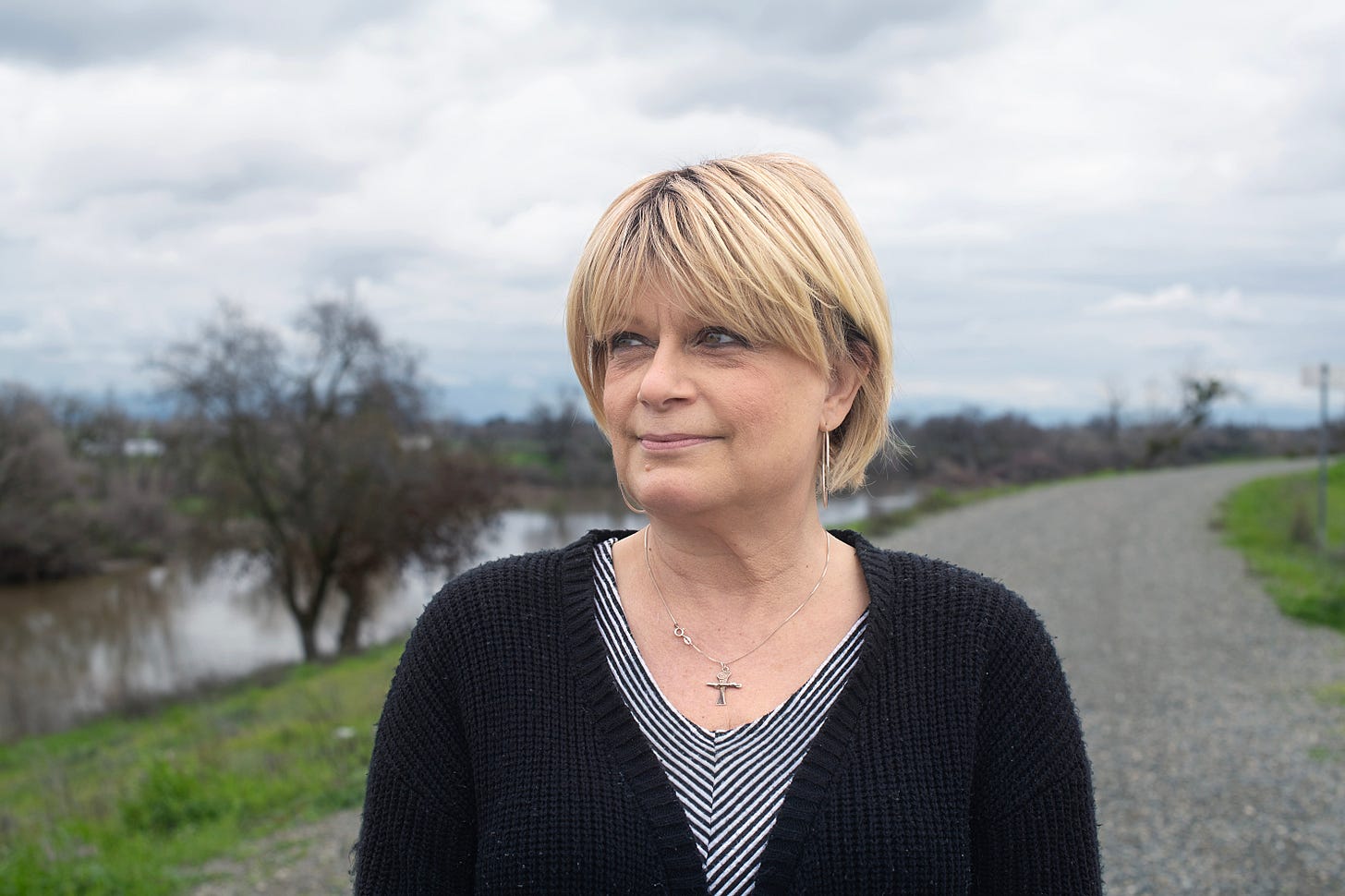 A medium closeup of a woman with short blonde hair wearing a striped tshirt, black cardigan and a silver cross around her neck A medium closeup of a woman with short blonde hair wearing a striped tshirt, black cardigan and a silver cross around her neck