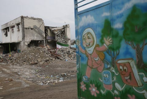 A school building very badly damaged after a bombing. In the foreground is a mural showing a girl in a headscarf walking in a country scene with two books with legs accompanying. A school building very badly damaged after a bombing. In the foreground is a mural showing a girl in a headscarf walking in a country scene with two books with legs accompanying.
