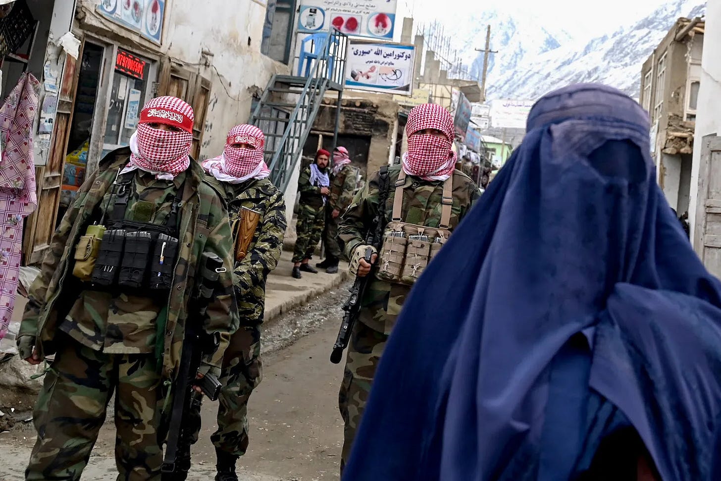 Taliban security personnel stand guard as an Afghan burqa-clad woman (right) walks along a street.
