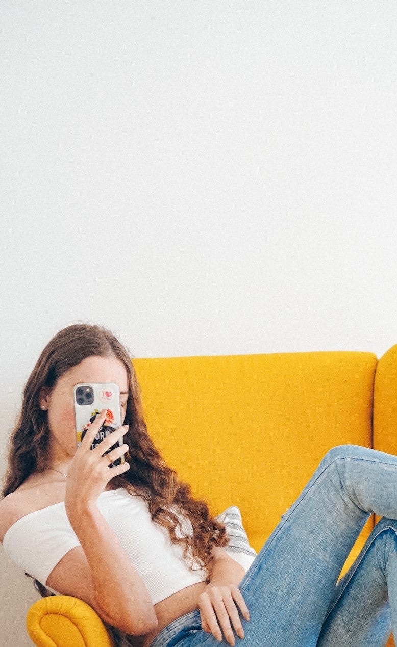 woman in white tank top and blue denim jeans sitting on yellow sofa woman in white tank top and blue denim jeans sitting on yellow sofa