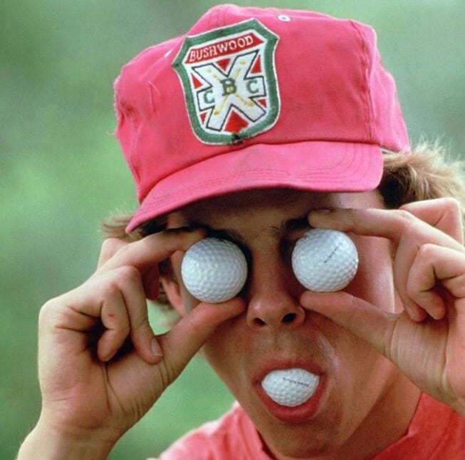 This may contain: a person wearing a red hat and holding golf balls in front of their eyes with both hands This may contain: a person wearing a red hat and holding golf balls in front of their eyes with both hands