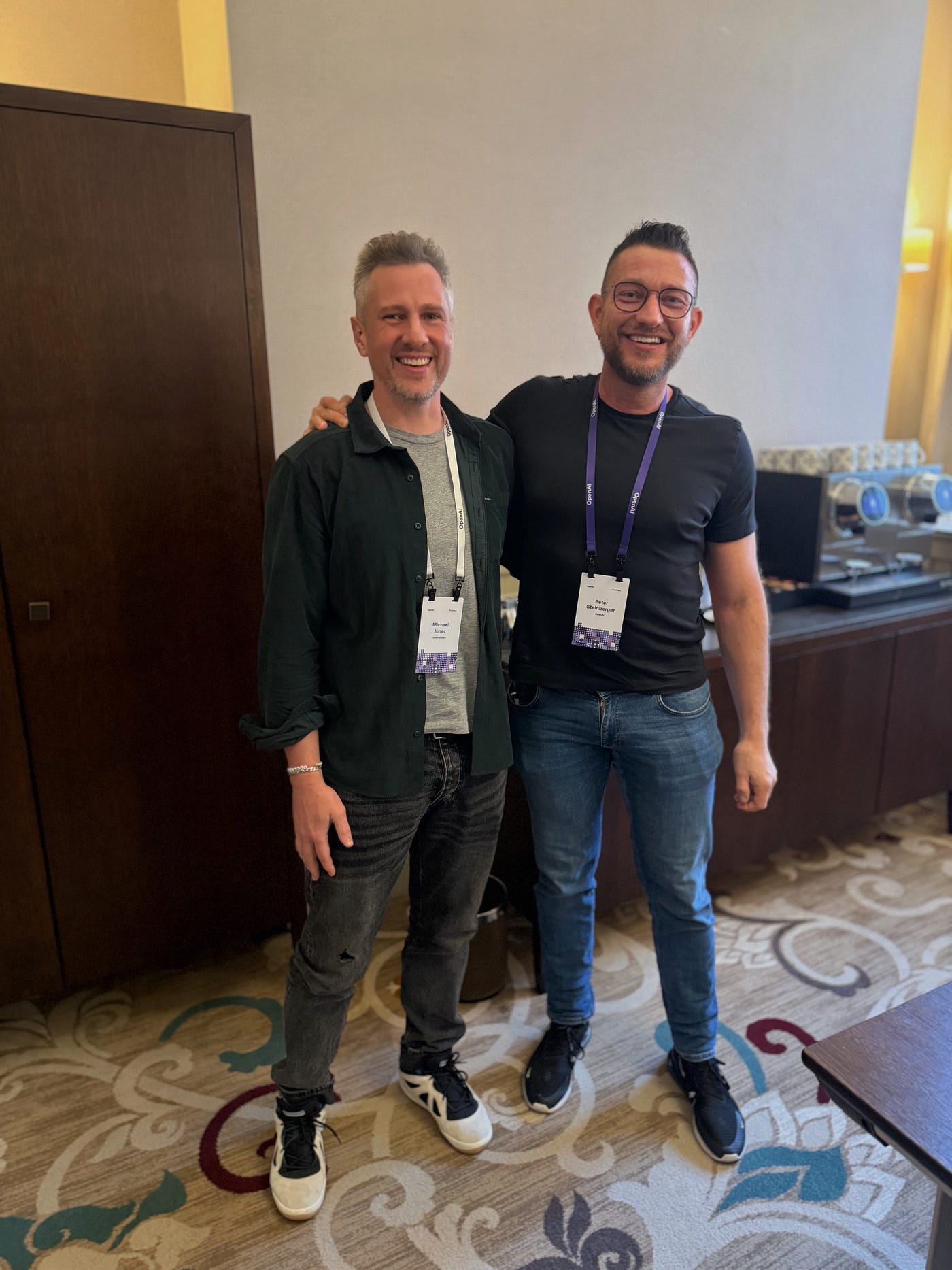 Mike Jones (left, in dark shirt) stands with Peter Steinberger (right, in dark shirt with glasses) at what appears to be a conference venue, both smiling. Mike Jones (left, in dark shirt) stands with Peter Steinberger (right, in dark shirt with glasses) at what appears to be a conference venue, both smiling.