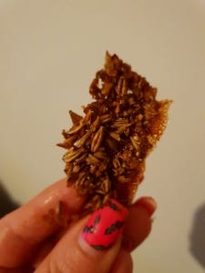 photo of the malt biscuit, a brown malt cracker, looks like a very thin granola bar. held by a woman's hand with painted nails