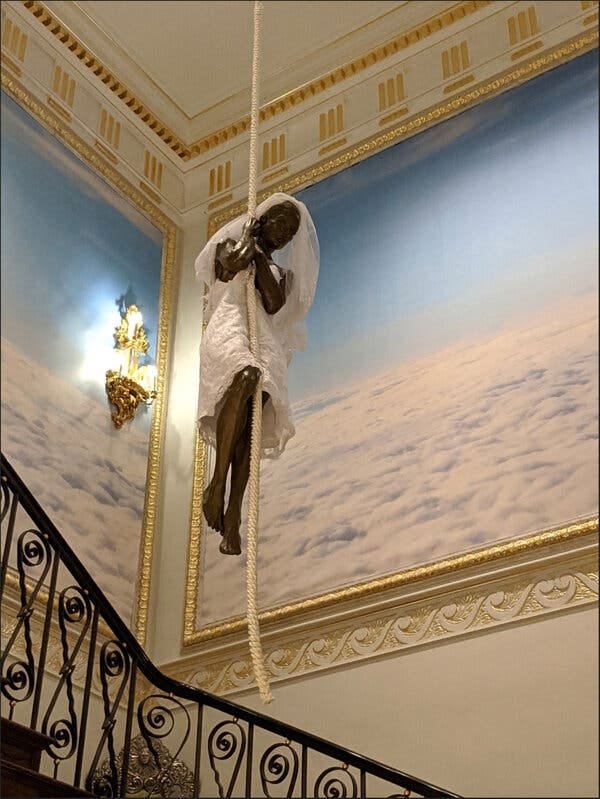 A stairwell with a wrought-iron banister, enormous gilt-framed paintings of clouds on the walls and a suspended sculpture of a bride clinging to a rope. A stairwell with a wrought-iron banister, enormous gilt-framed paintings of clouds on the walls and a suspended sculpture of a bride clinging to a rope.