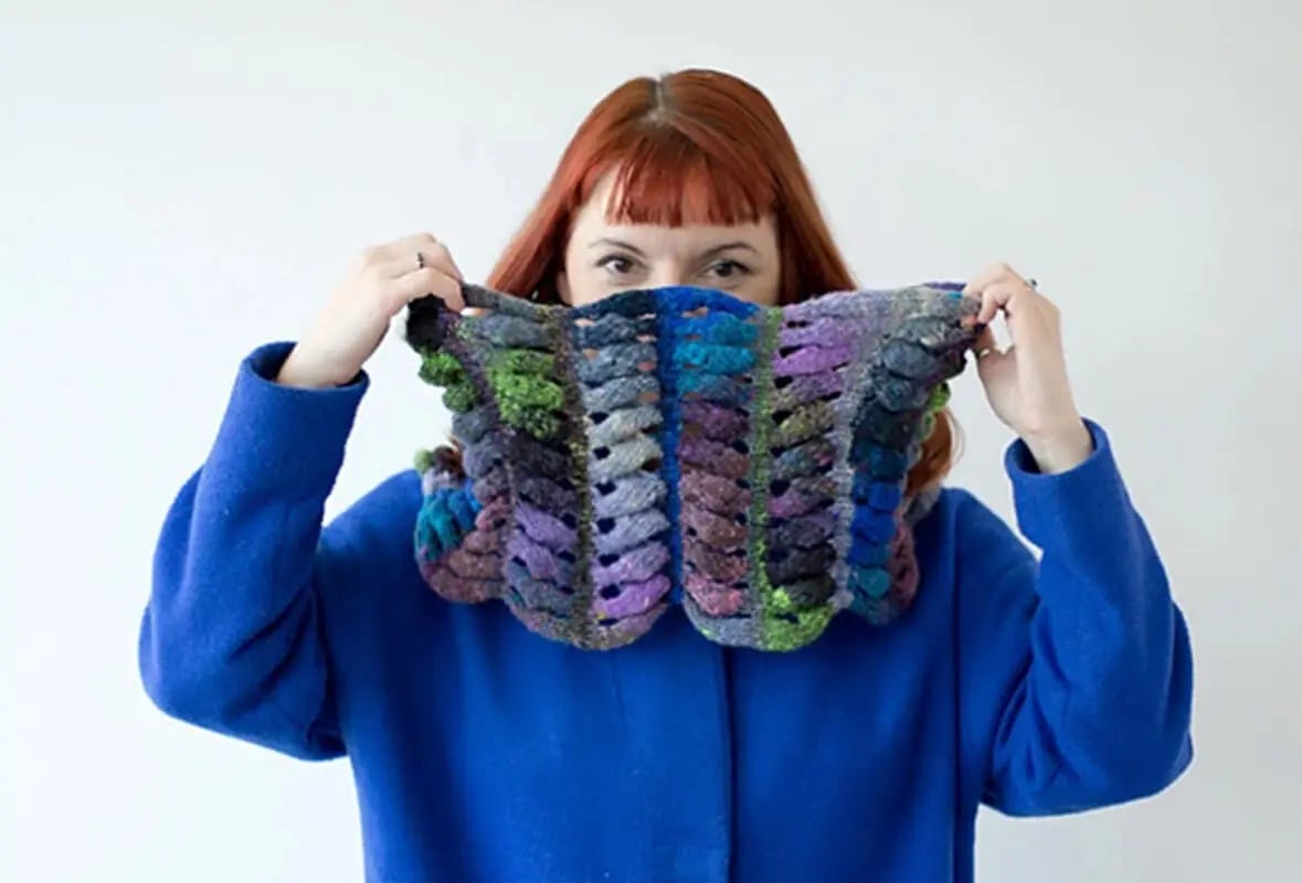 red-haired woman wearing a colorful knitted cowl and a blue coat 