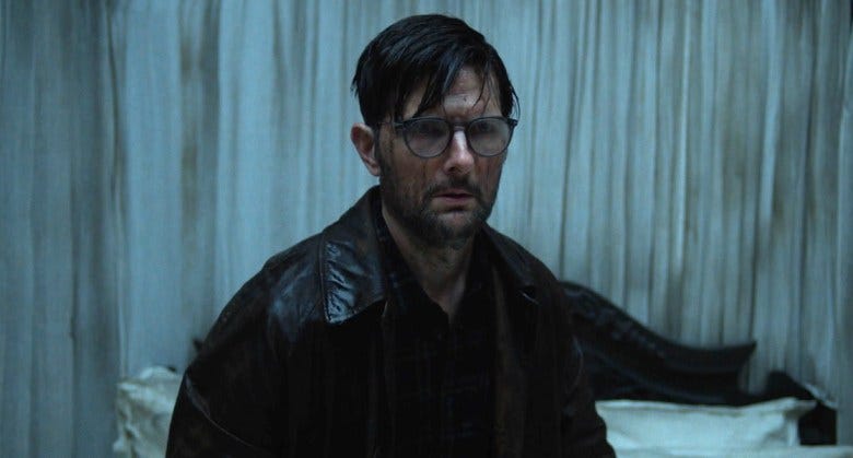 A still from the horror film "Hokum," in which actor Adam Scott stands in a bedroom, looking wet. 