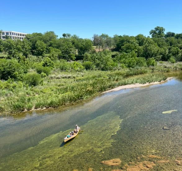 Author and daughter in canoe on the Colorado River, office building visible behind the treeline