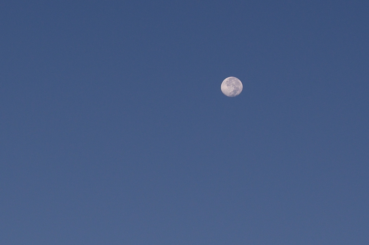 The full moon setting in the blue morning sky