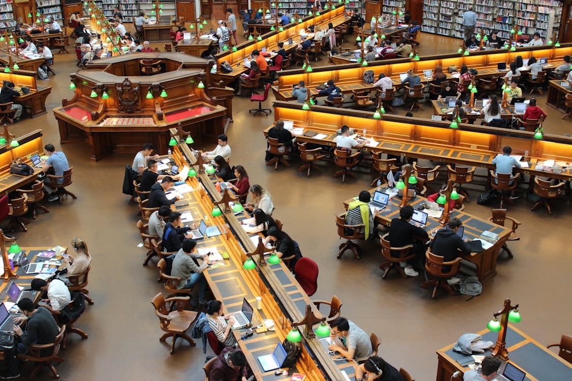 Free A lively university library scene with students studying diligently at wooden desks. Stock Photo