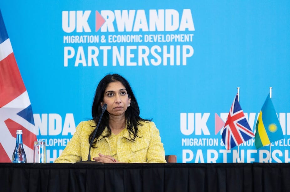 Suella Braverman sitting at a table in front of a blue wall that reads UK Rwanda migration and economic development partnership Suella Braverman sitting at a table in front of a blue wall that reads UK Rwanda migration and economic development partnership