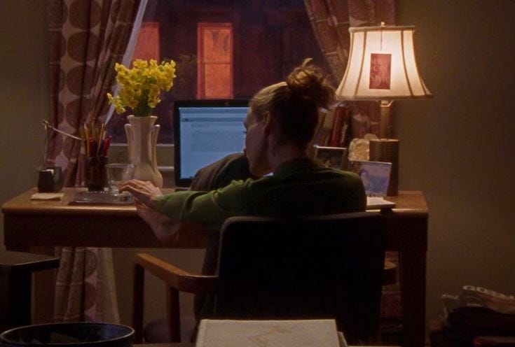 This may contain: a woman sitting at a desk with a laptop computer in front of her and flowers on the table