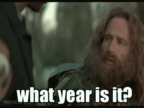 A meme of a man with a wild beard frantically asking what year it is.