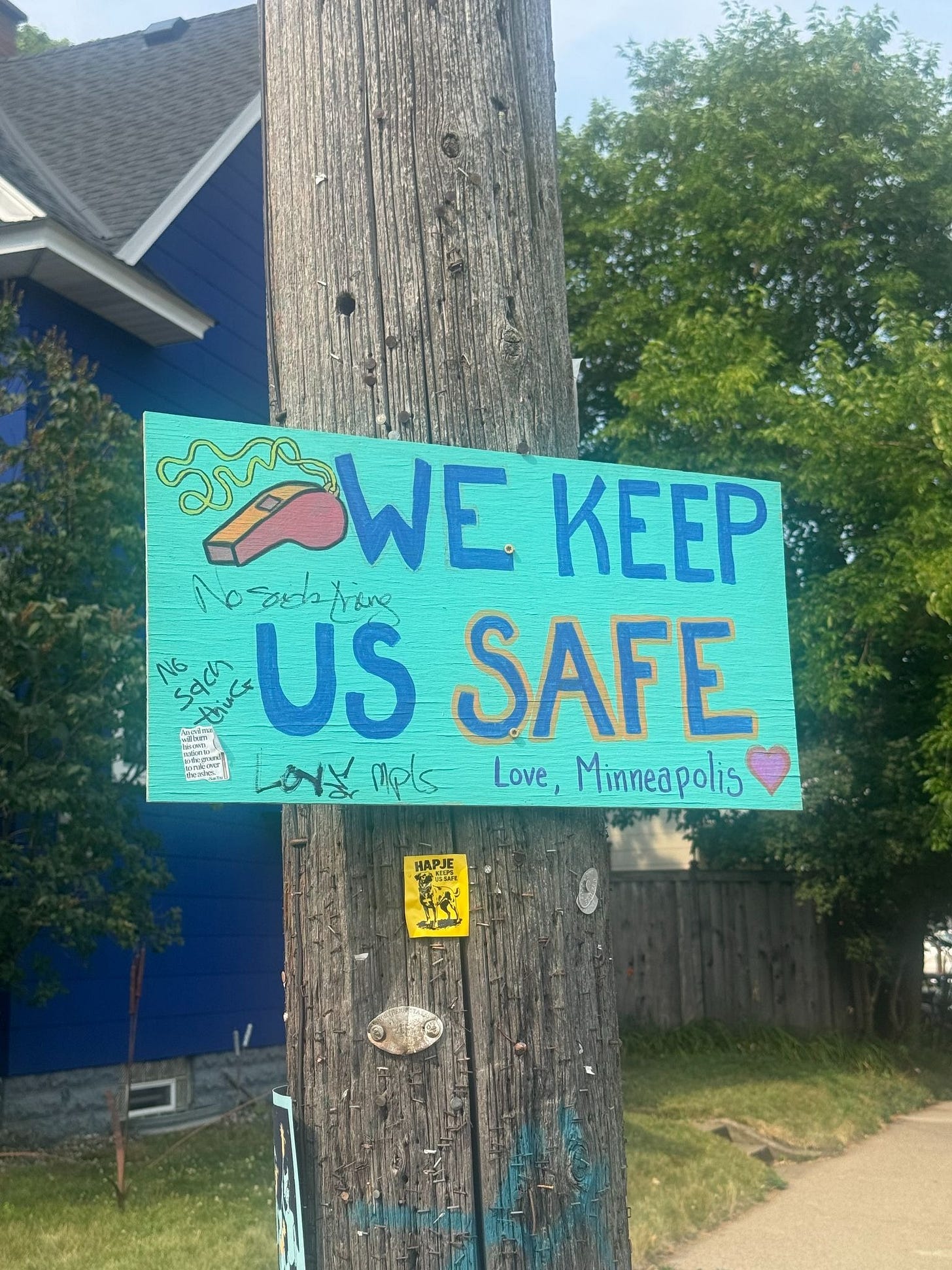 Homemade sign on a telephone pole with a drawing of a whistle. Text says "WE KEEP US SAFE Love, Minneapolis"