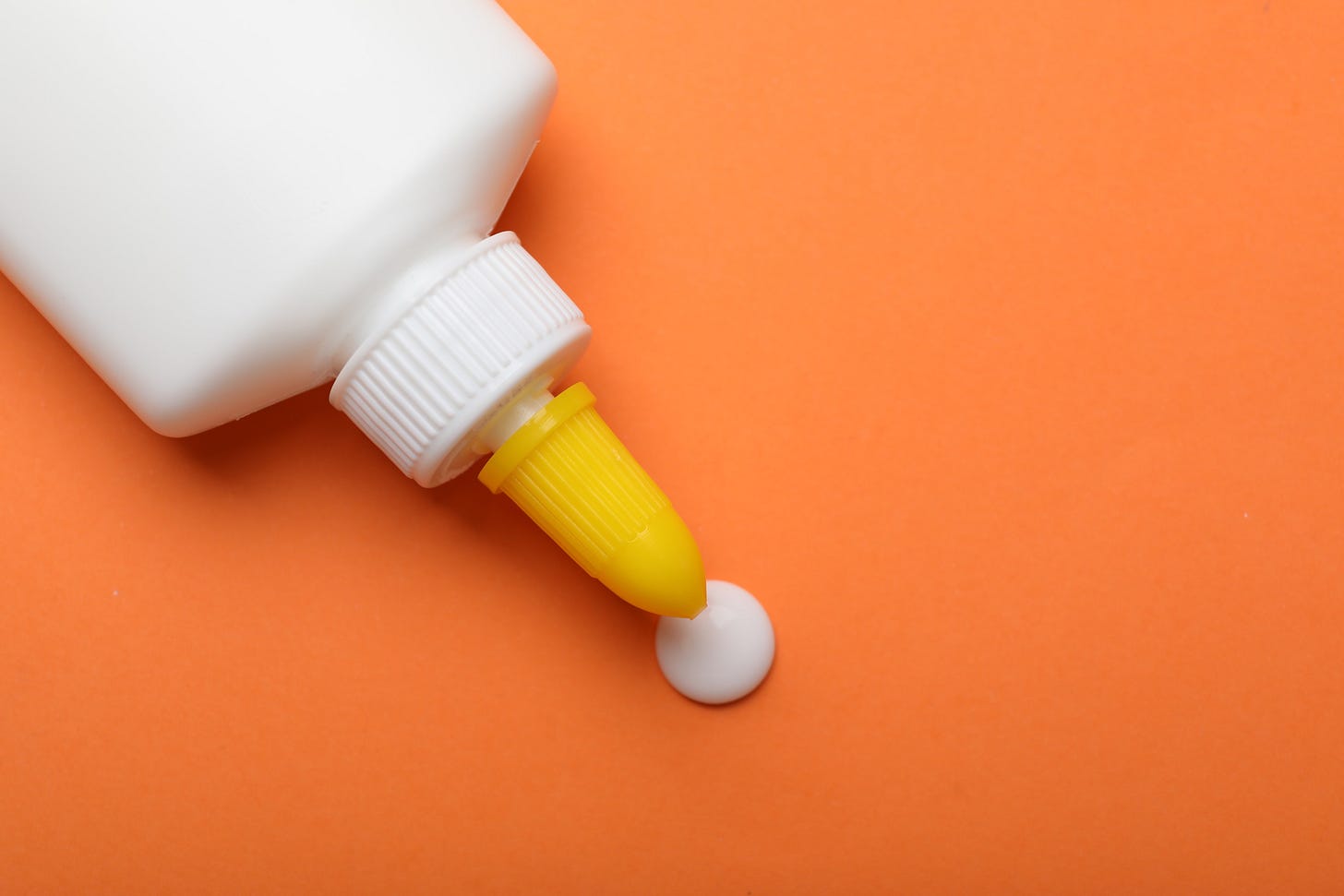 Picture of white glue bottle putting some white glue on an background of orange