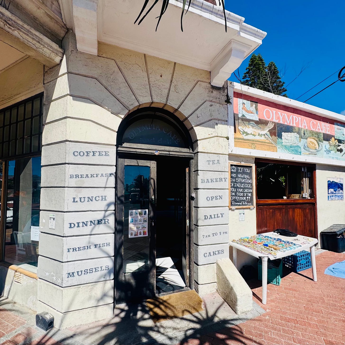 Entrance of Olympia Café in Kalk Bay, South Africa, with its front door open to the street, inviting people inside.